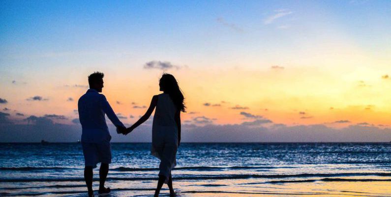 Honeymoon - Man and Woman Holding Hands Walking on Seashore during Sunrise