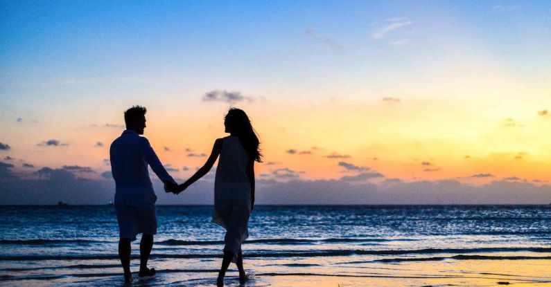 Honeymoon - Man and Woman Holding Hands Walking on Seashore during Sunrise